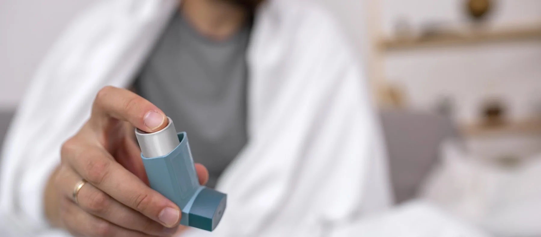 A person sitting up in bed holding out a reliever inhaler