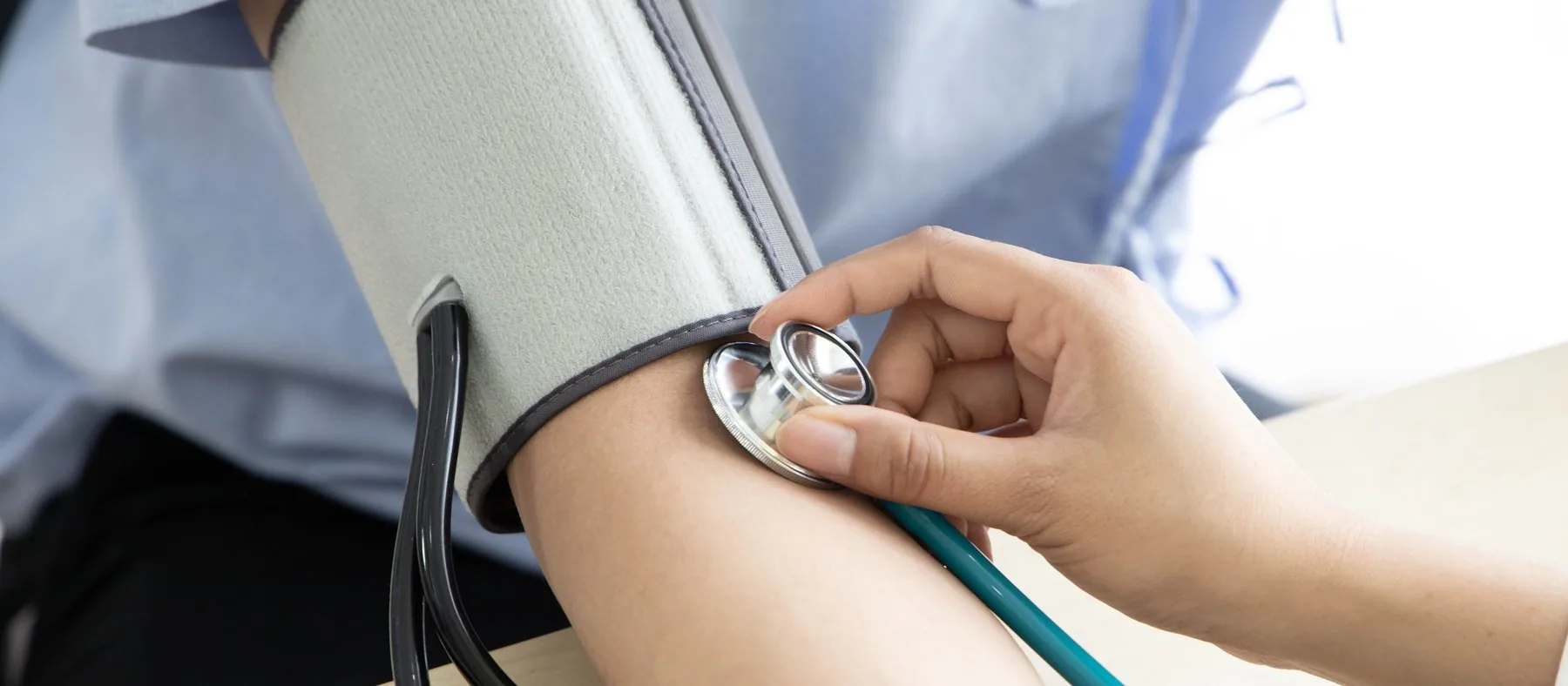 A blood pressure cuff on a patient’s upper arm, with a stethoscope held below it