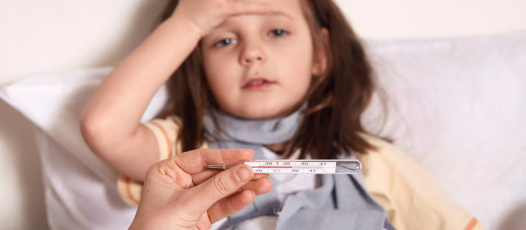 A parent holding a thermometer beside a child resting in bed