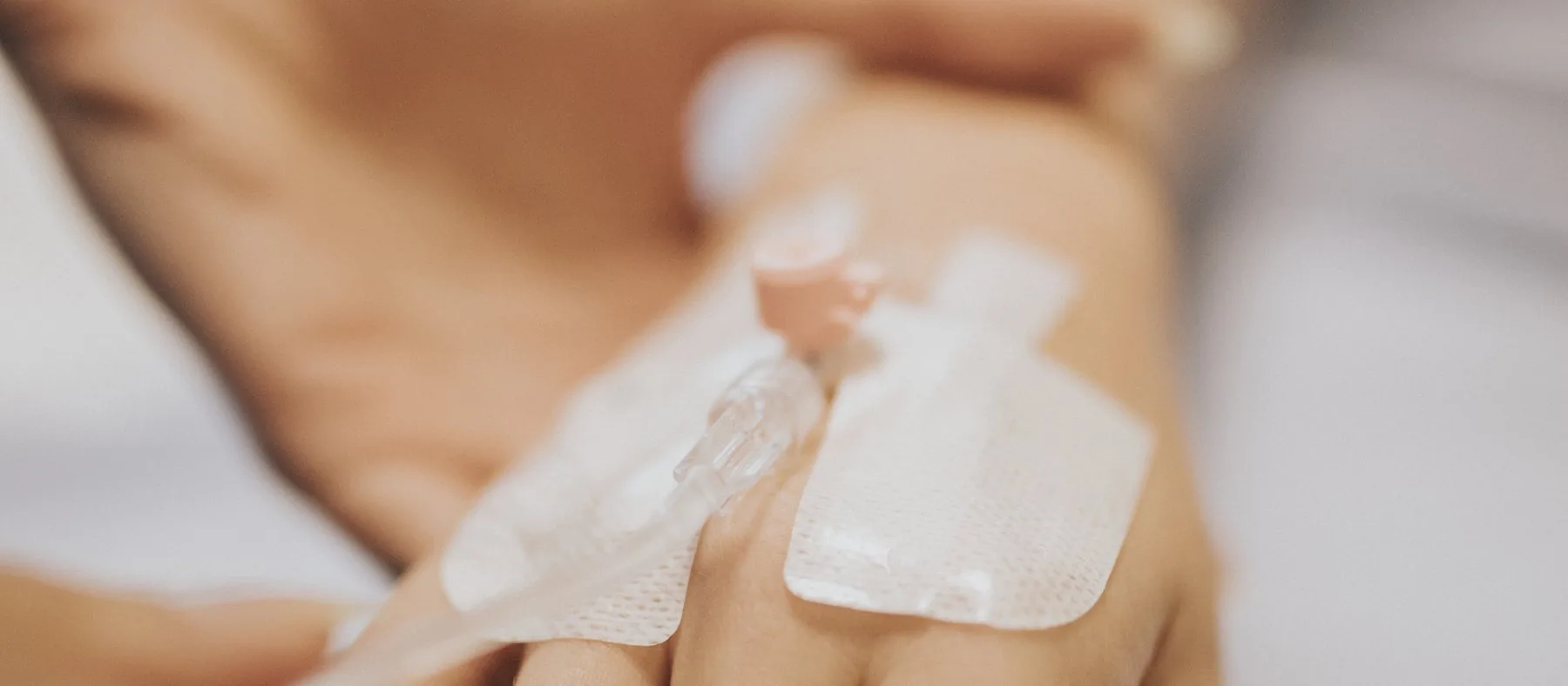 A cannula taped to the back of a patient's hand, held by a nurse