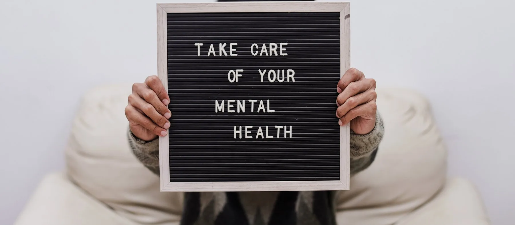 A person holding a letterboard reading “take care of your mental health”