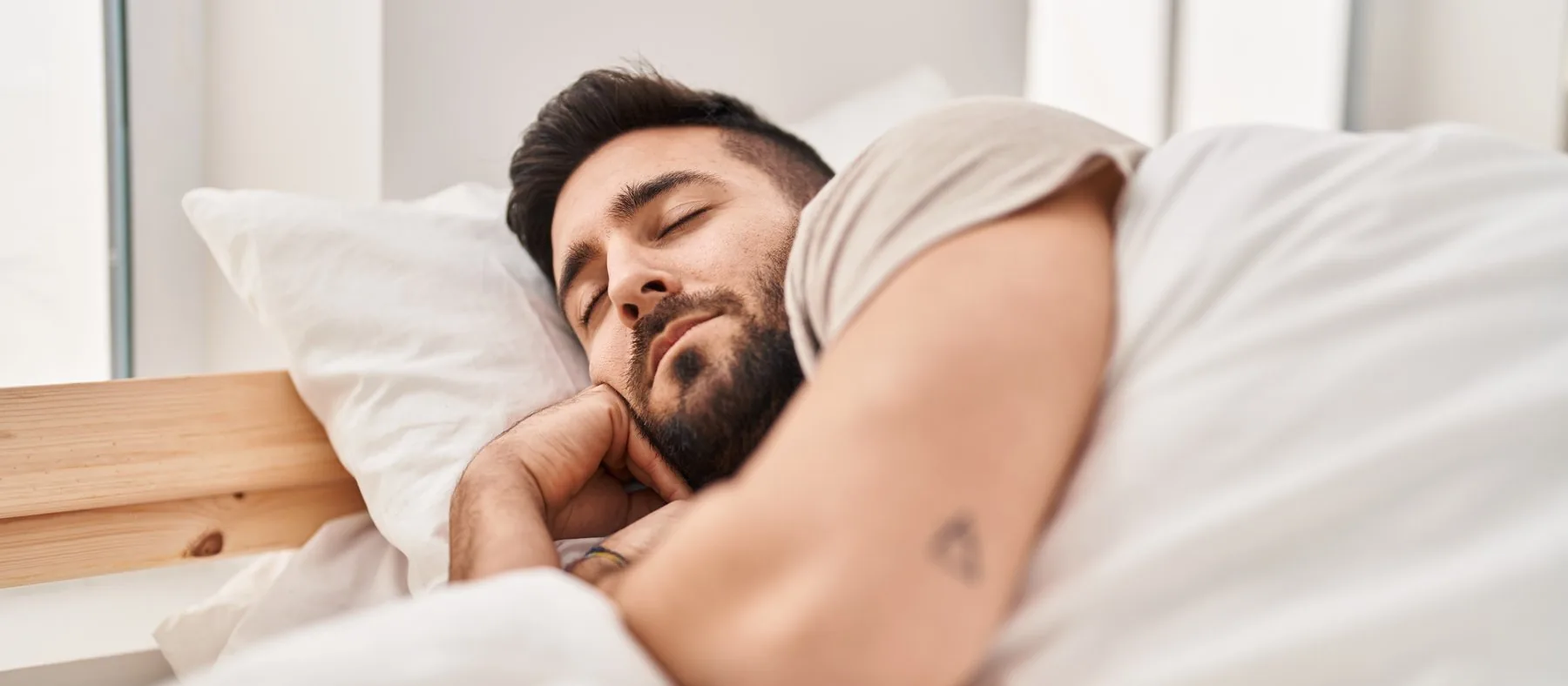 A man asleep in bed in a bright, daylit bedroom